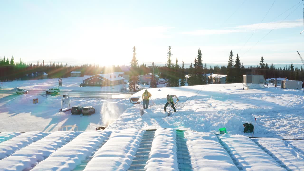 Two men shoveling the snow off the roof of a local business warehouse in Soldotna, Alaska