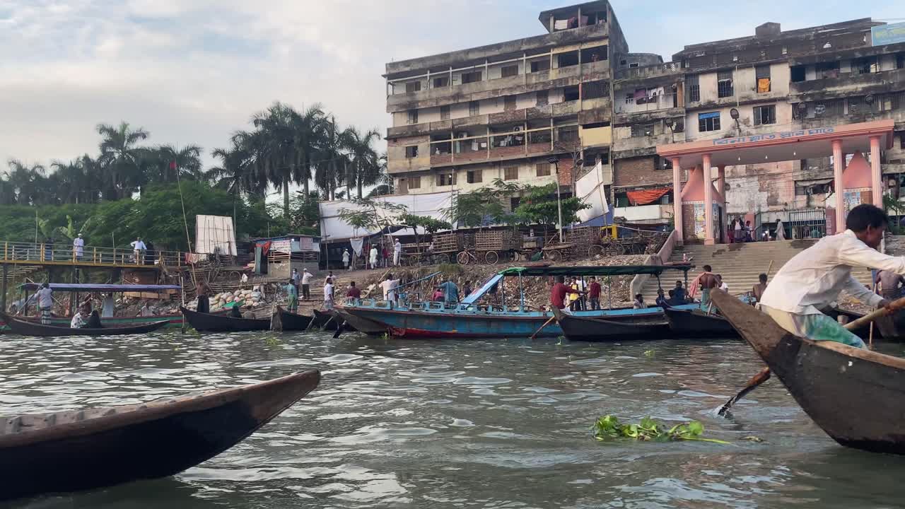 boatmen await passengers on banks of Buriganga river, in old Dhaka. old city buildings in background