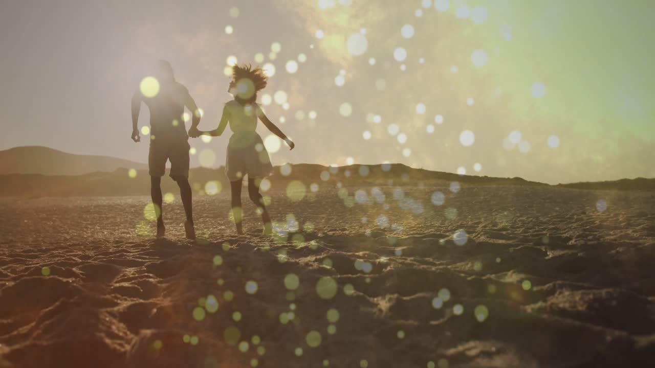 Coppia che cammina sulle dune al tramonto e corre mano nella mano, immortalando un viaggio romantico con effetto bokeh.