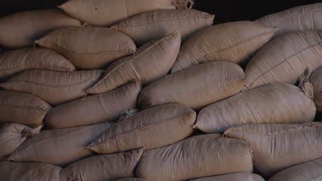 stacked burlap bags filled with processed ilex paraguariensis yerba mate leaves stored inside warehouse during post-processing phase, packed tightly creating repetitive patterns