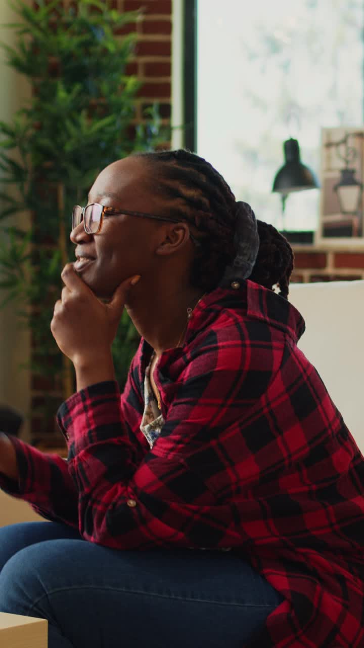 Vertical video: Smiling woman eating pizza and watching tv show