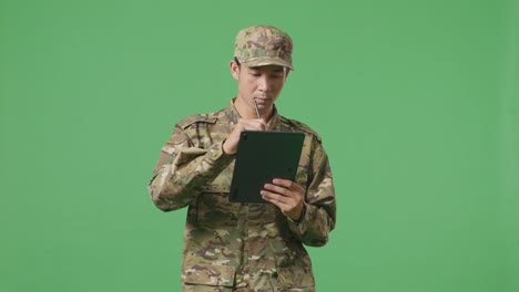 un soldado asiático tomando notas en una tableta mientras camina en el estudio de fondo de la pantalla verde