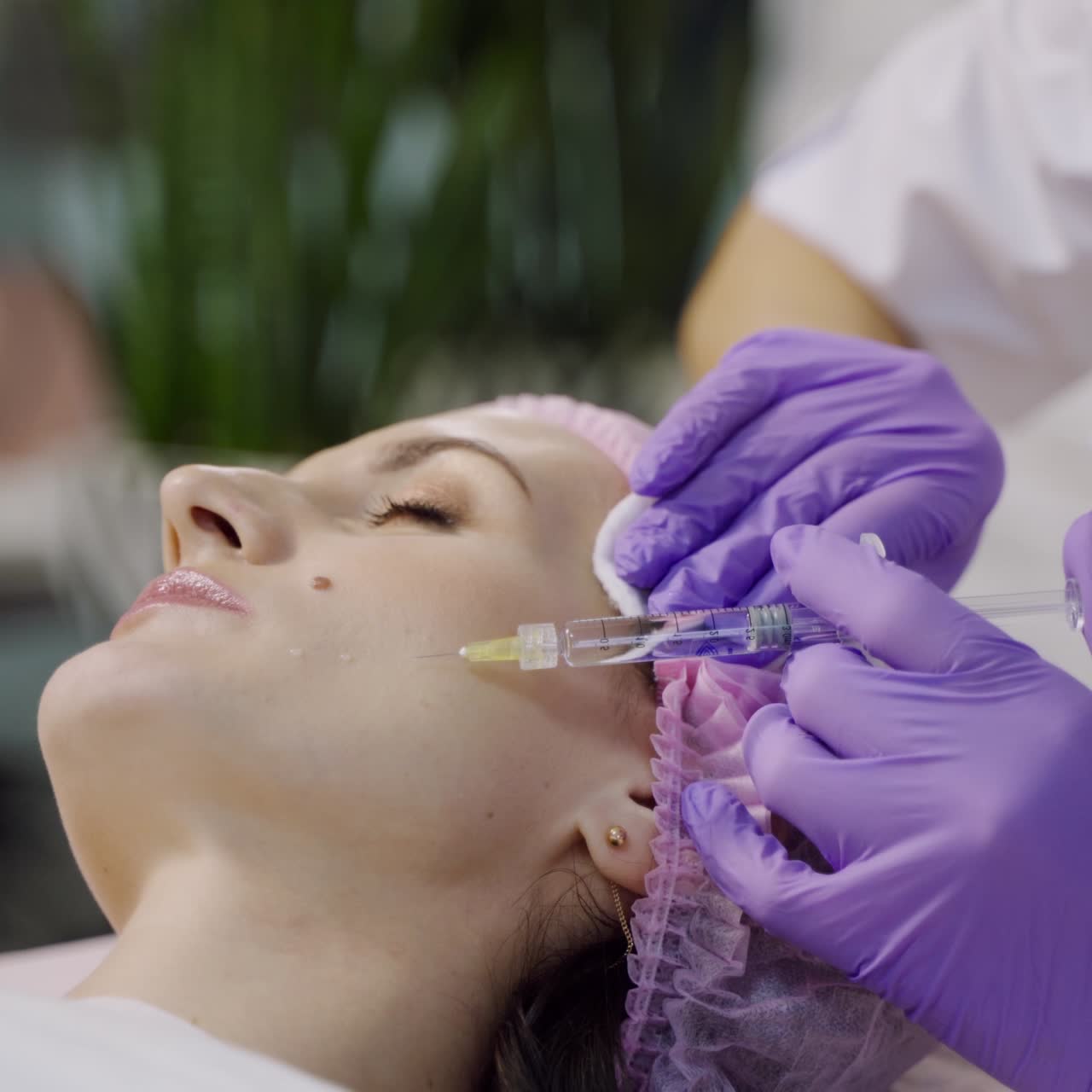 An experienced cosmetologist conducts mesotherapy for a woman who lays on a couch in the cosmetology office. Close-up