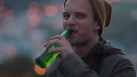 retrato atractivo hipster hombre bebiendo alcohol en el techo sonriendo con confianza disfrutando de un estilo de vida exitoso en la ciudad urbana al atardecer