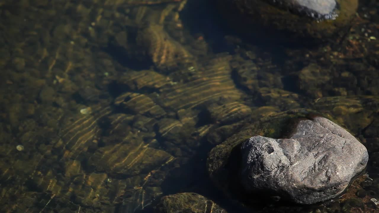 Acqua che crea increspature attorno a rocce con ciottoli sotto l'acqua bassa