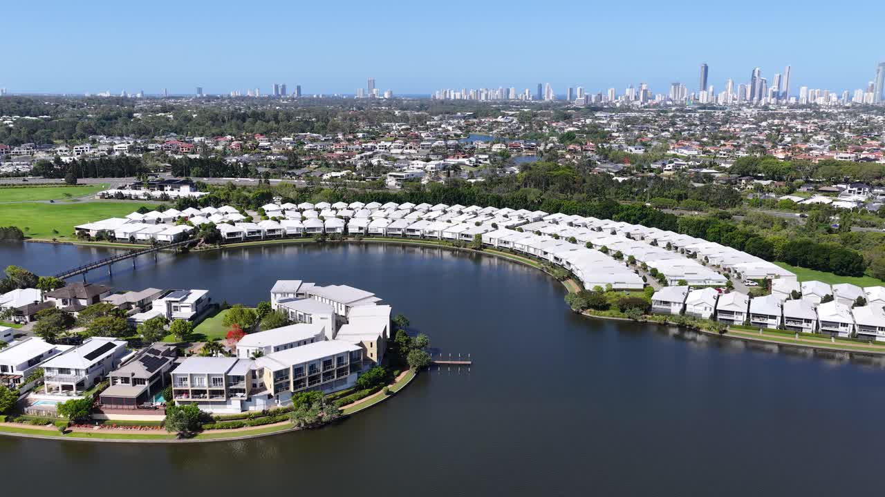 Drone che sorvola un complesso residenziale curvo sul lungolago con skyline della città in lontananza in una giornata di sole