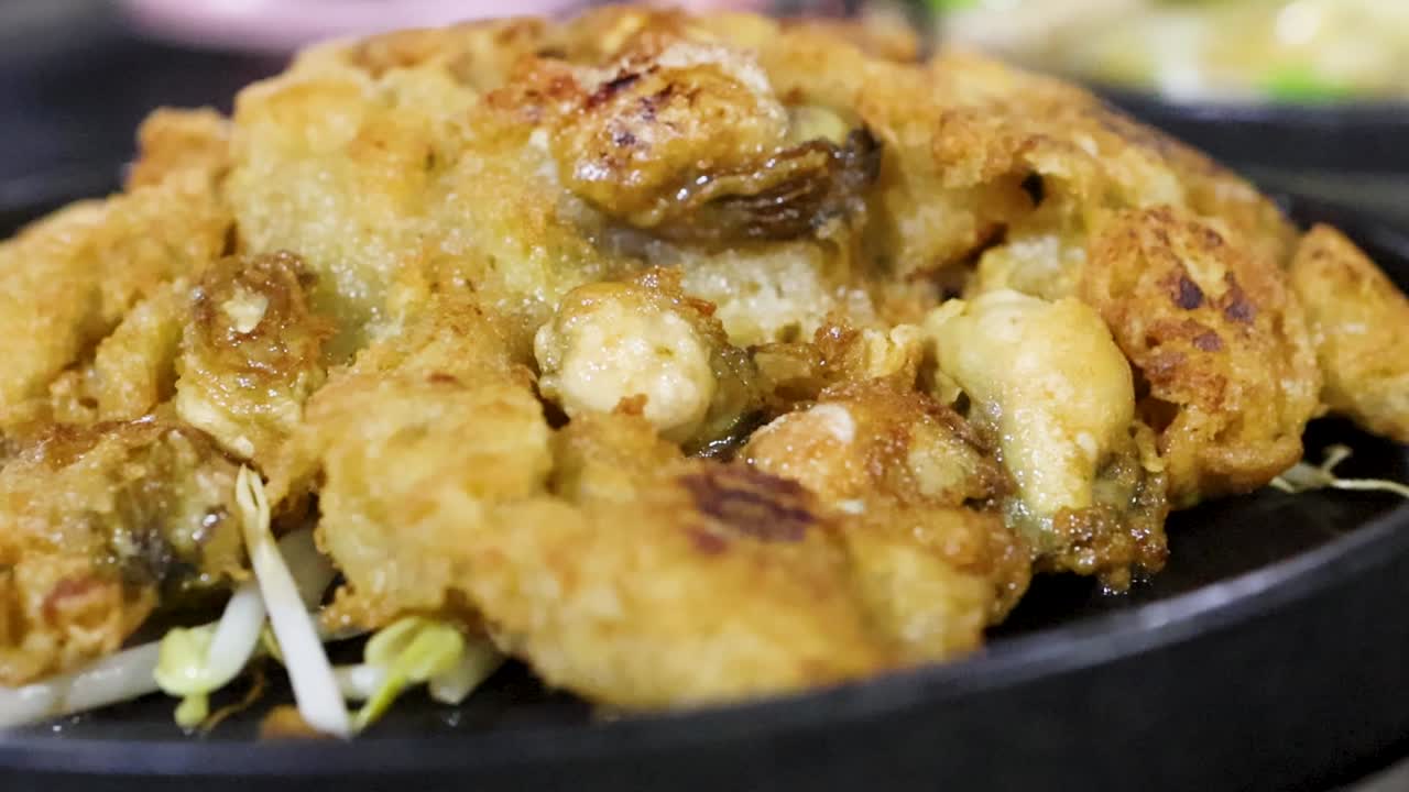 Close-up detail pancake tiram goreng keemasan dengan tauge di atas wajan hitam