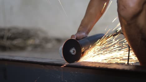 a construction worker is cutting metal with a grinder without using gloves and safety equipment