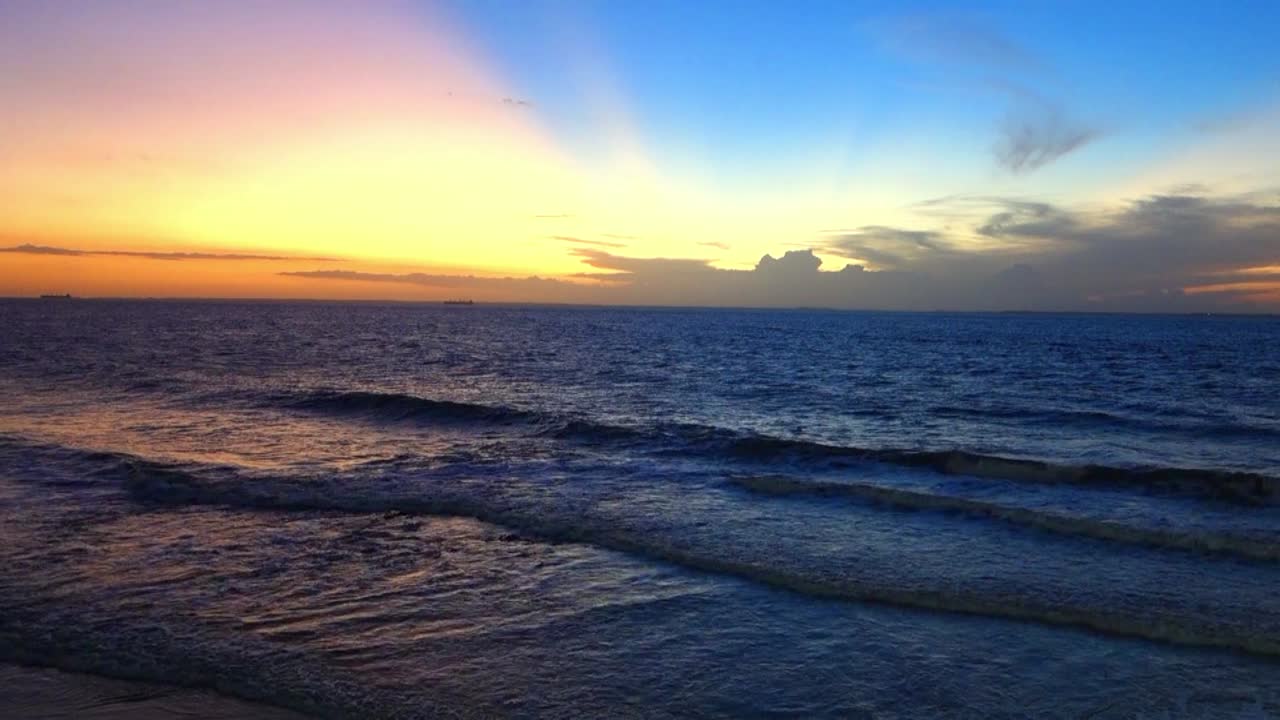 Big tide waves with foam and splashes are crushing beach with stones and rock in slow motion during beautiful warm yellow sunset in ocean. 4K close up.Sun dawn ocean silhouette paradise island.