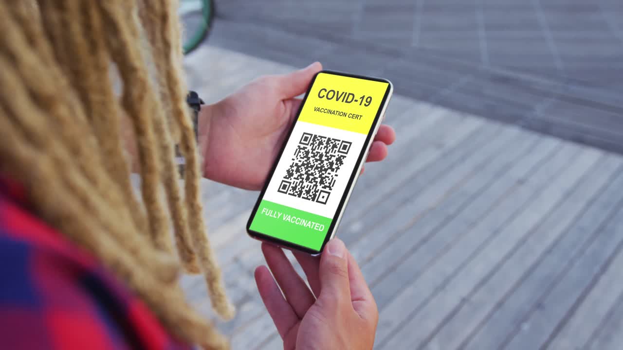 Man with dreadlocks holding smartphone with covid vaccination certificate and qr code on screen