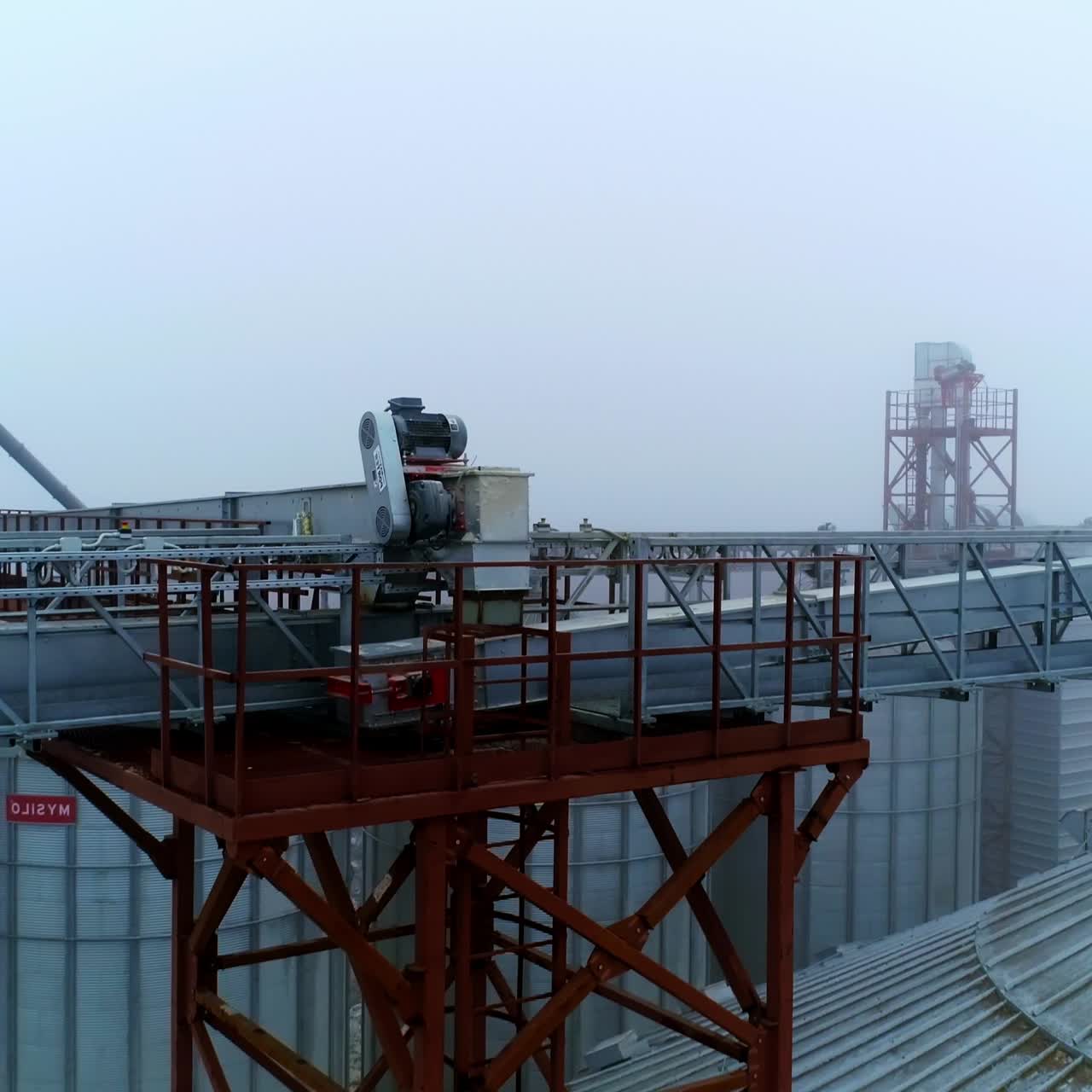 Metal beams on the tops of silo tanks joining them together. Moving along the beams in foggy weather. Misty air in the backdrop