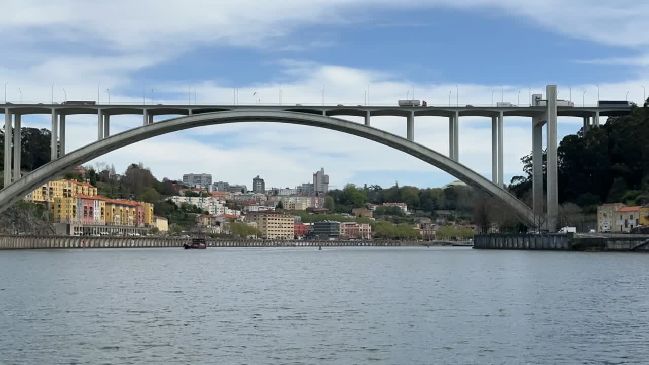 Time lapse of traffic moving across Ponte Infante Dom Henrique in Porto, Portugal. Arched concrete bridge spans Douro River with colorful riverside buildings and hills in the scenic background