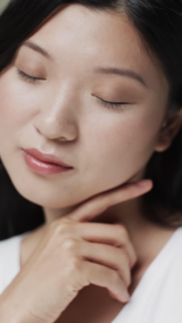 Vertical video of asian woman with black hair and make up touching face, copy space, slow motion