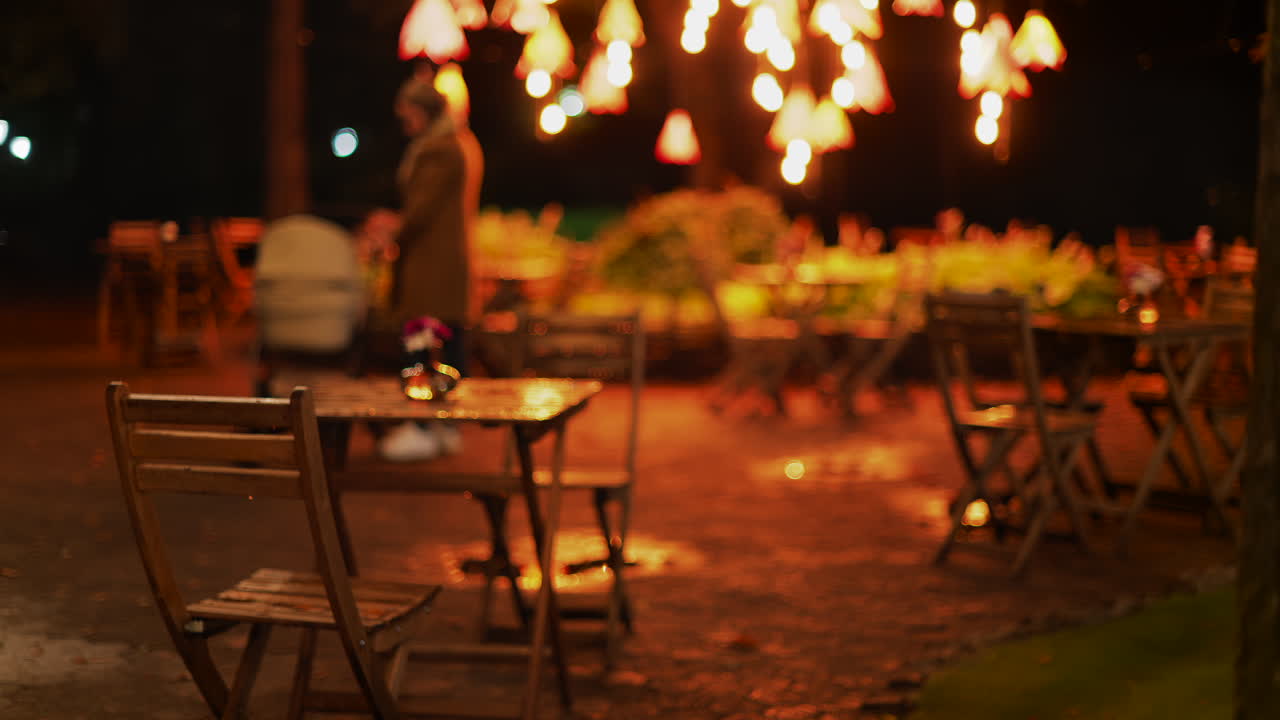 A cozy outdoor cafe at night with glowing warm lights and wooden chairs glistening after rain