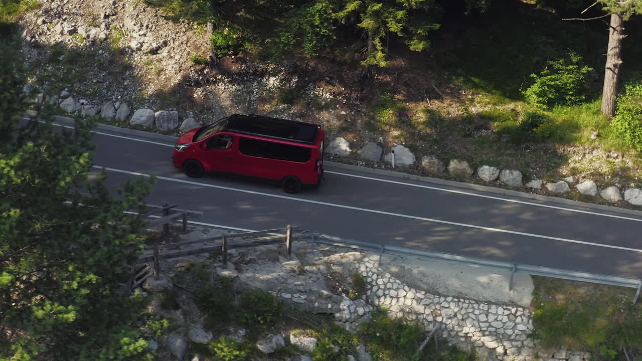 Un minivan rosso spunta da dietro gli alberi mentre percorre una strada di montagna attraverso la foresta.