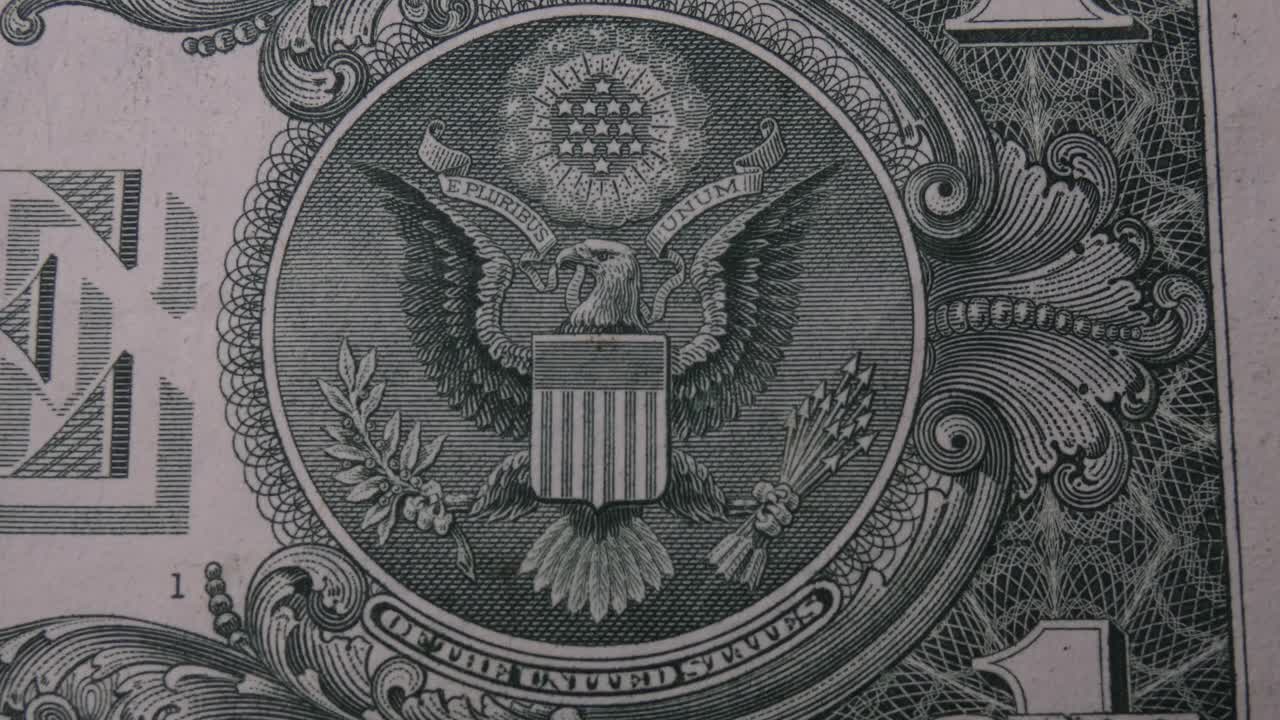 The great seal on the back of a 1 U.S. Dollar bill. The banknote moves and pans from left to right and stops on the bald eagle emblem