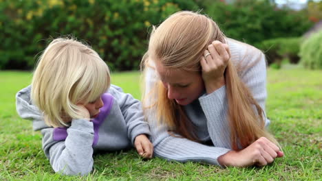 mother and daughter lying on grass talking