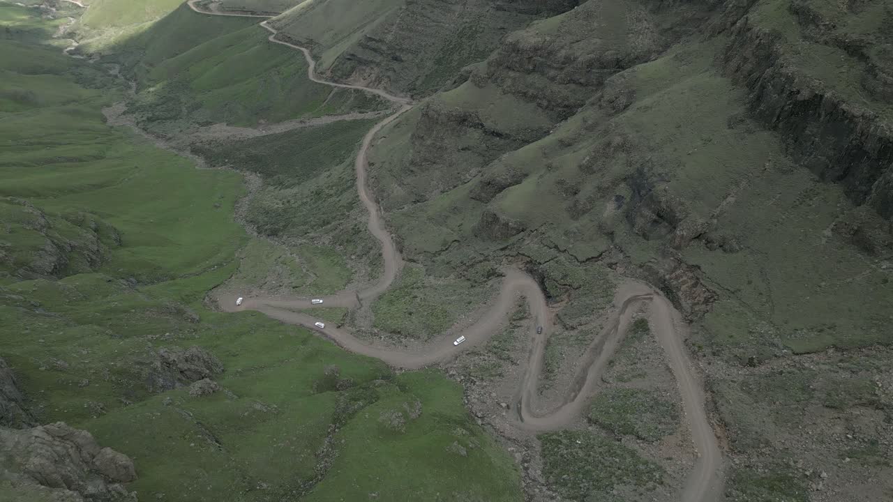 пять внедорожников спускаются по крутой грунтовой дороге в труднопроходимом горном перевале