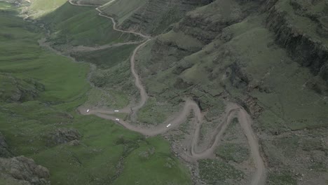 Five-SUVs-descend-steep-dirt-switchback-road-in-rugged-mountain-pass