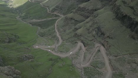 cinco vehículos todoterreno descienden por un empinado camino de tierra en un escarpado paso de montaña