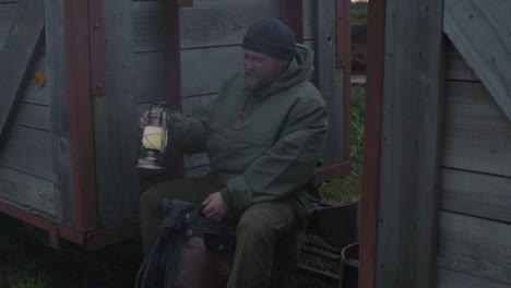 Man-in-wilderness-with-lamp-and-backpack-making-break-between-wooden-train-wagon