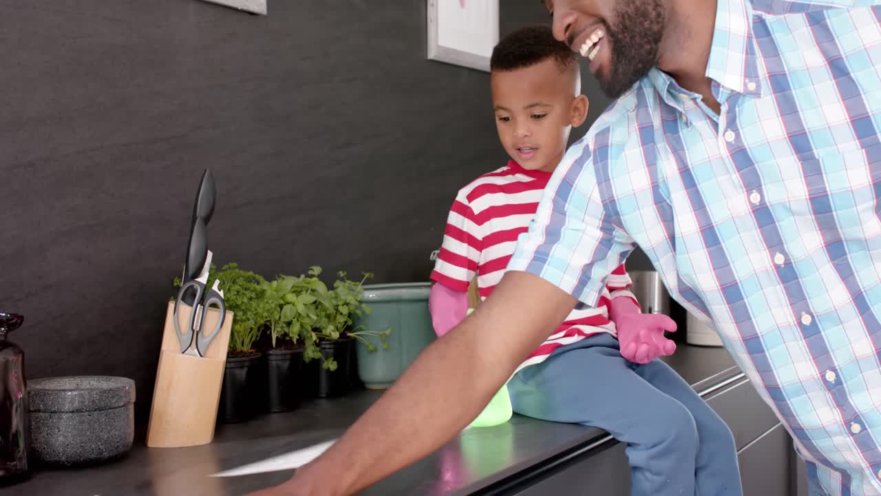 feliz padre y hijo afroamericanos limpiando y haciendo high five en la cocina, en cámara lenta