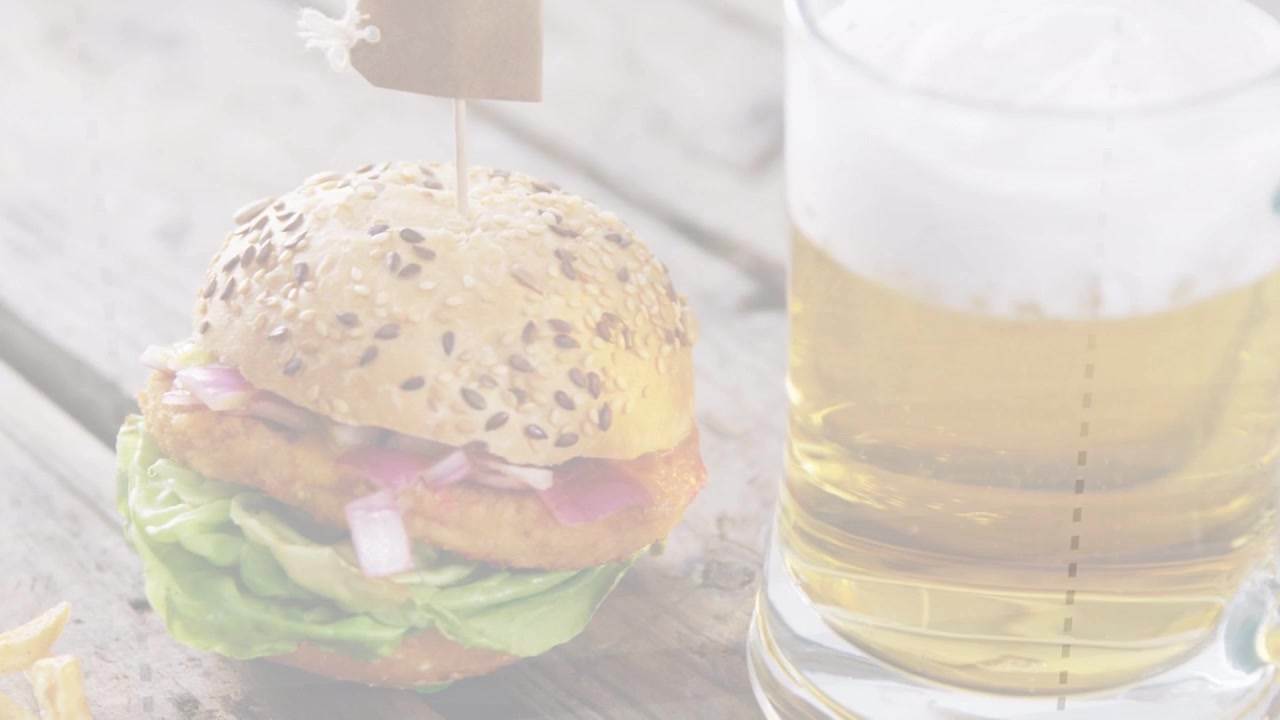 Telecamera che si sposta a sinistra, rivelando un hamburger con panino ai semi e spiedino, patatine che appaiono, birra che mostra il pasto.