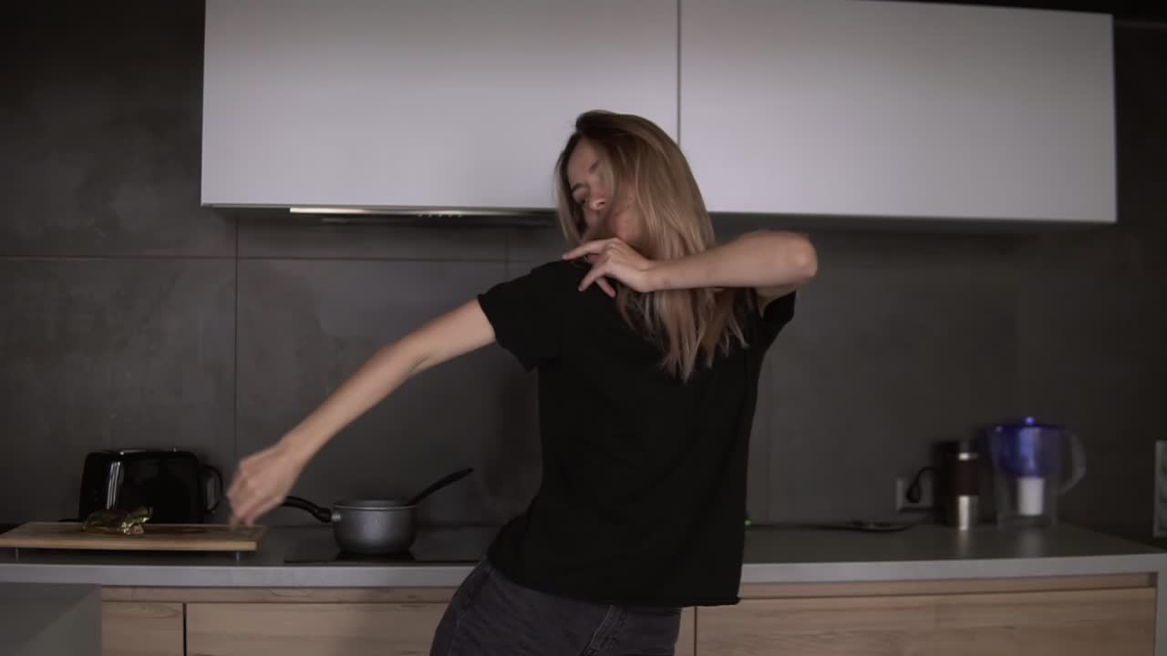 La ragazza balla con movimenti sinuosi in cucina, con interni in stile loft moderno.