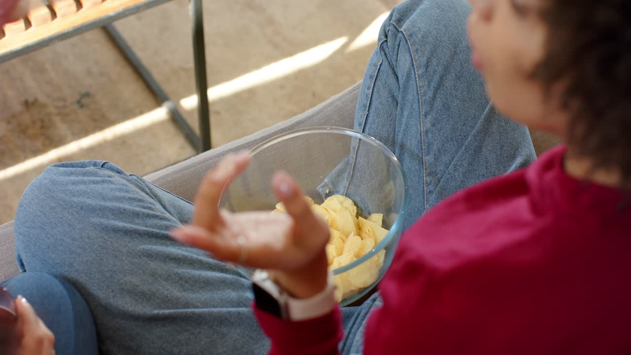 Amigas diversas segurando bebidas enquanto outras pegam petiscos em uma tigela de batatas fritas no pátio