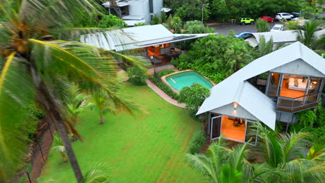 aerial drone of orbit descends around palm trees to large tropical staged estate with pool