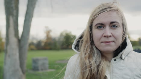 Portrait-of-a-young-pensive-woman-in-an-autumn-park.-Standing-in-a-jacket-with-a-hood-on-her-head