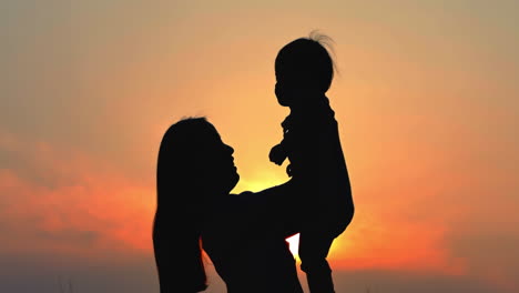 Eltern-Kind-Konzept,-Schöne-Mutter-Und-Kind-Vor-Sonnenorangefarbenem-Himmel,-Silhouette-Von-Mutter-Und-Baby-Im-Gegenlicht-Des-Sonnenuntergangs,-Familienurlaubsabenteuer,-Aktiver-Gesunder-Lebensstil