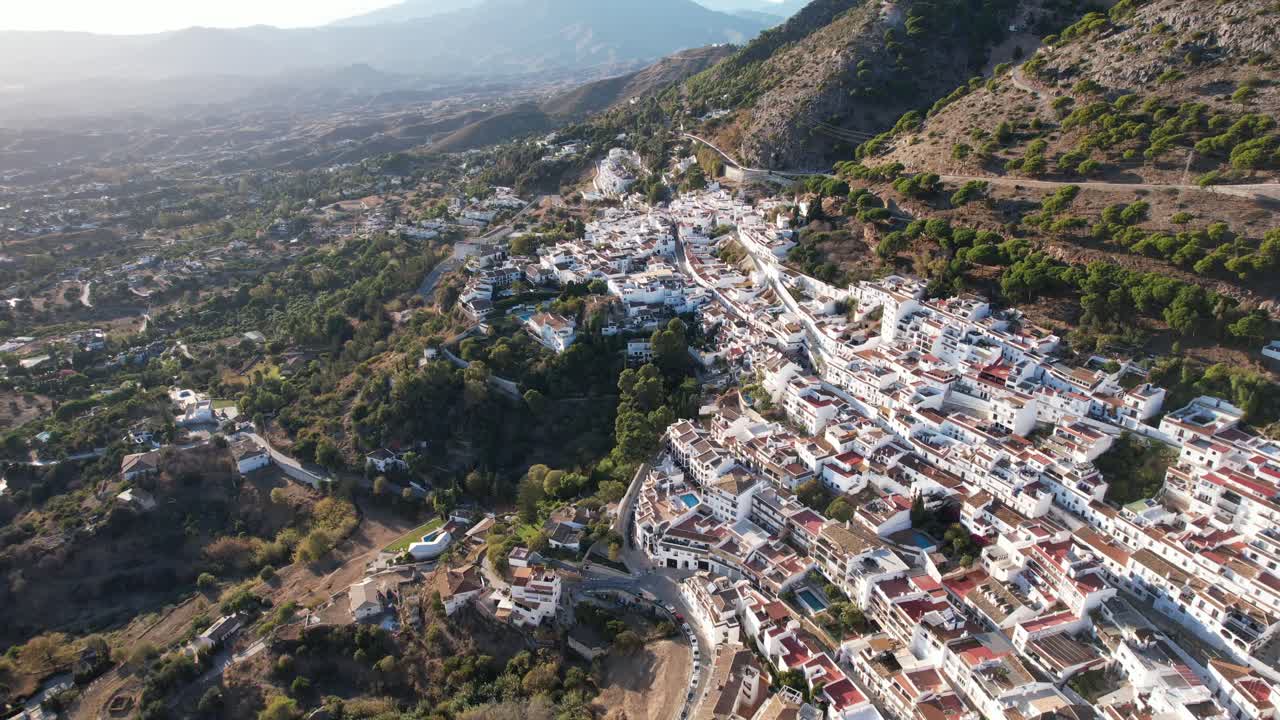 Aerial tilt down reveals green mountains and winding streets and white homes of mijas pueblo spain