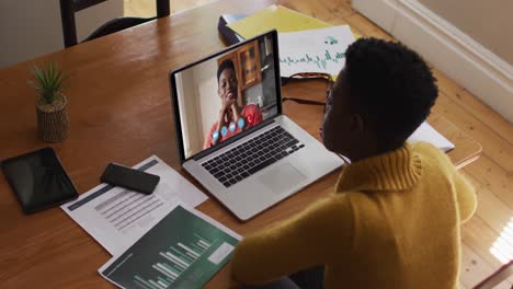 mujer afroamericana que usa una computadora portátil en una videollamada con una colega que trabaja desde casa