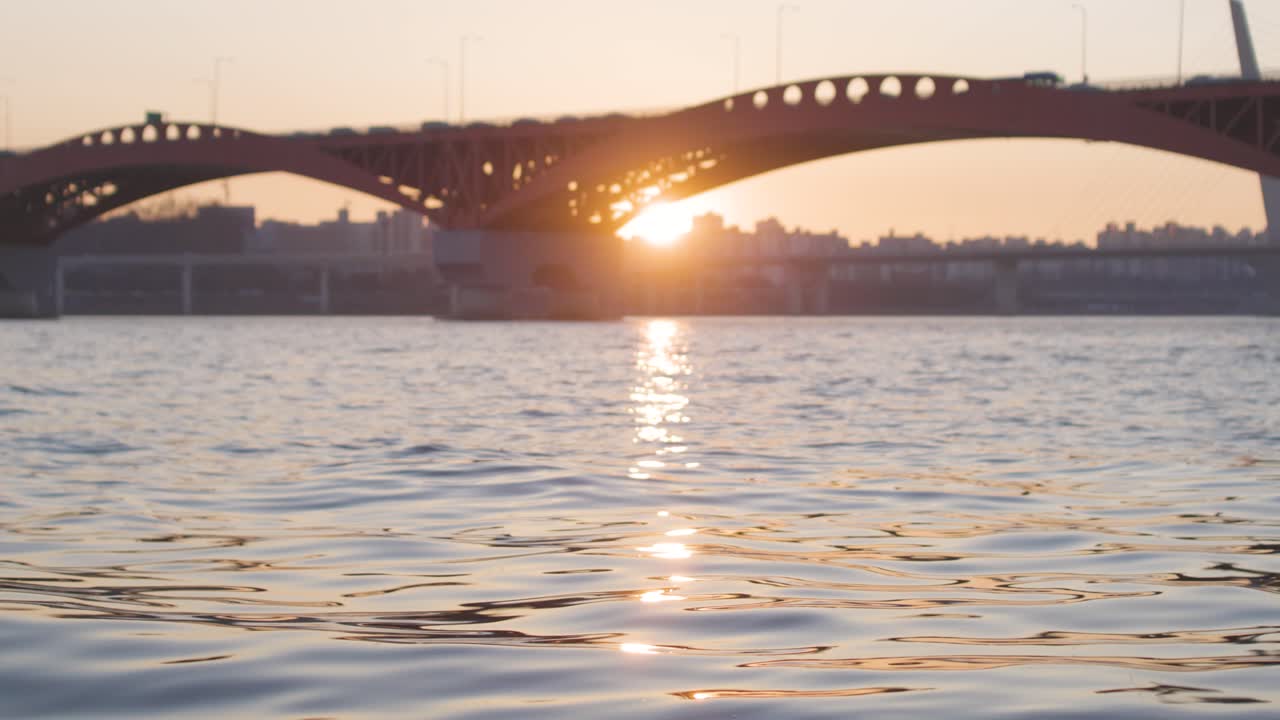 The sun sets under a large industrial bridge over a large body of water in South Korea.