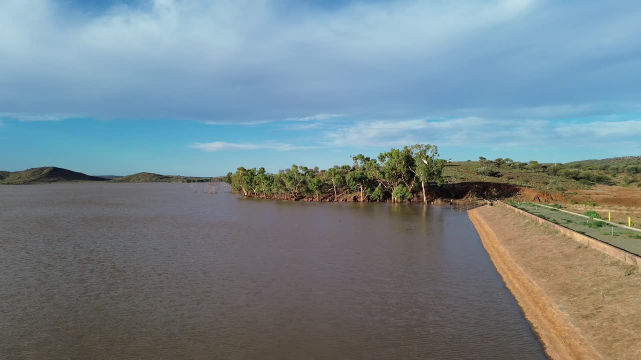 volando a lo largo de la pared de una presa a través del agua hacia los árboles que bordean las orillas