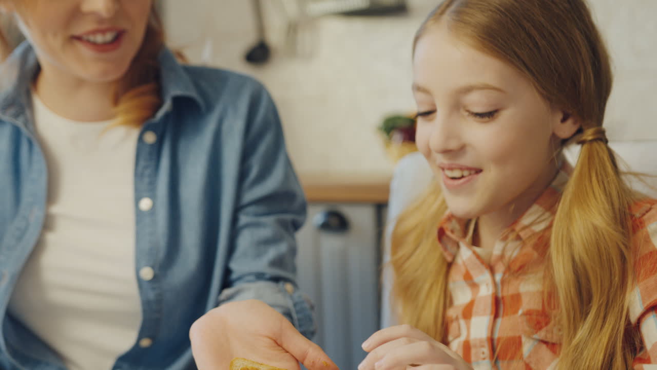 madre y hija sonrientes felices sentadas en la cocina y haciendo sándwiches con mantequilla de maní. de cerca. retrato. interior