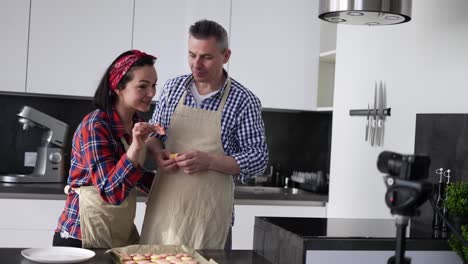 Pareja-Adulta-En-La-Cocina-Horneando-En-Casa,-Hablando-Ante-La-Cámara-Y-Probando-Galletas