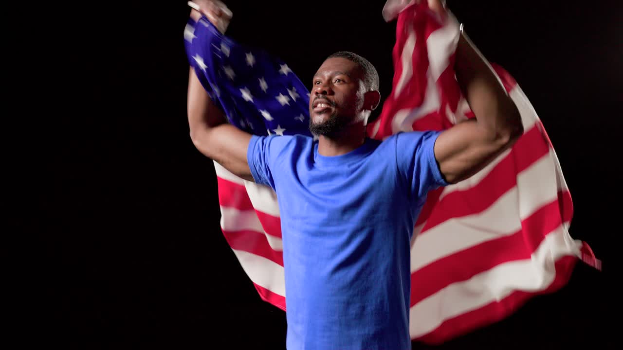 Uomo afroamericano che spiega, solleva e drappeggia la bandiera degli Stati Uniti all'inizio, mostrando orgoglio in studio con una maglietta blu.