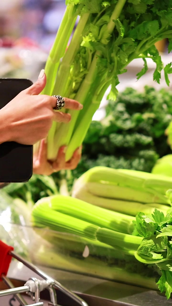 A shopper picks fresh celery from a supermarket display under bright lighting, capturing a routine grocery shopping moment