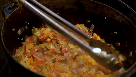 sausage and vegetable stir fry in pot, stirred with tongs