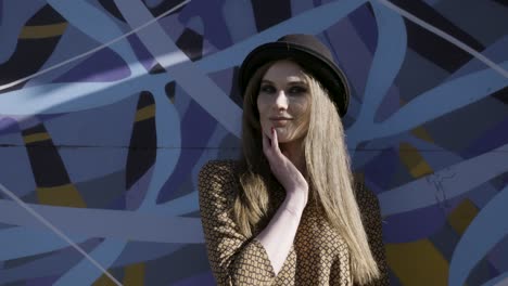 woman in a hat, posing in front of a graffiti wall