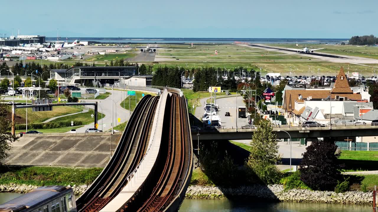 A SkyTrain Travels Along an Elevated Track With Planes and Runways Visible in the Background Near YVR, British Columbia, Canada - Aerial Drone Shot