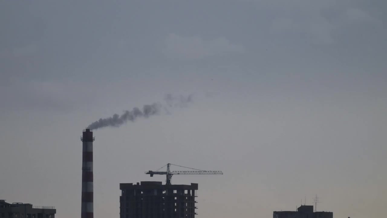 Time lapse of an industrial smokestack releasing emissions into the sky above a developing urban area