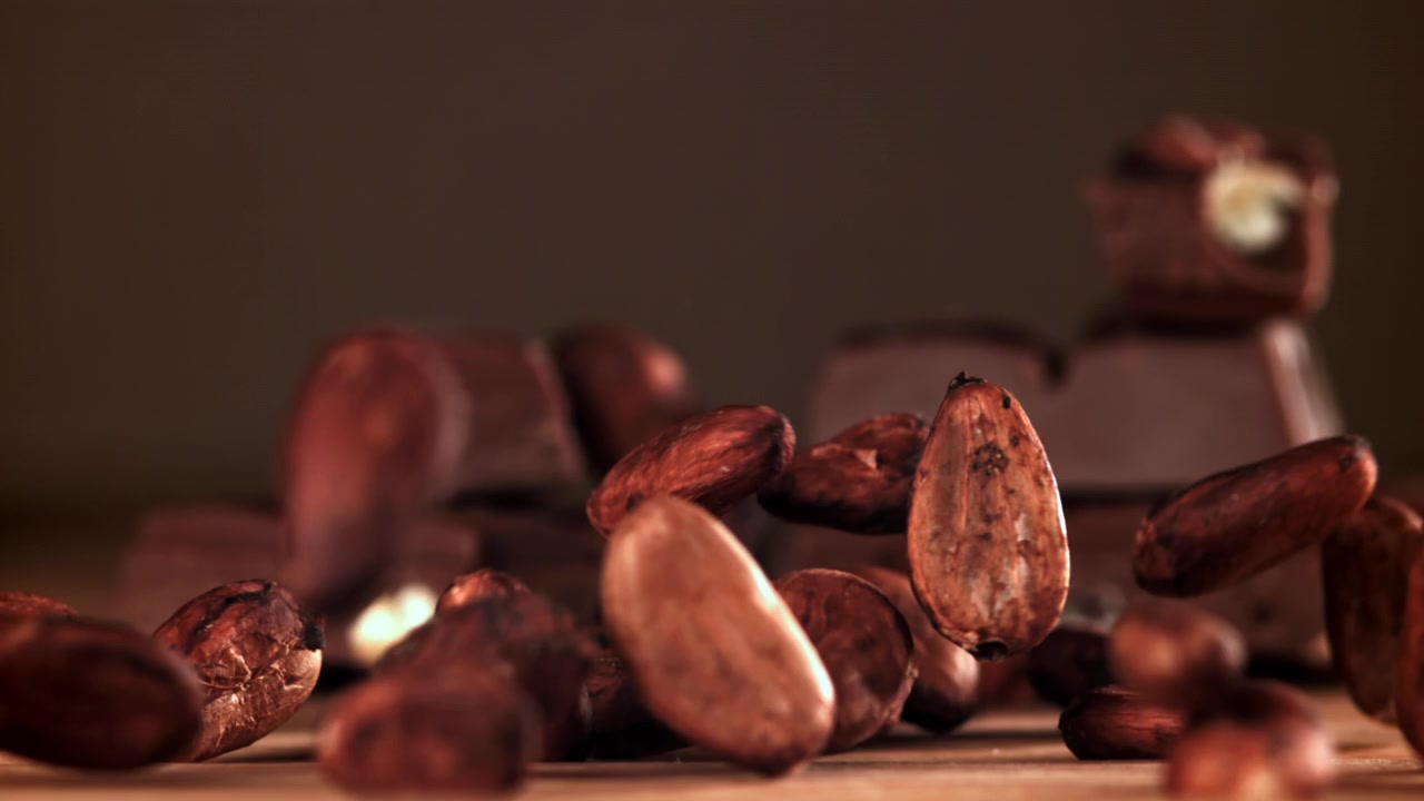 Cámara lenta de granos de cacao cayendo sobre una superficie de madera con tabletas de chocolate