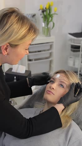 professional beautician in white uniform discussing skin treatment options with redhead female client lying on couch in modern beauty salon. concept of non-surgery cosmetology, professional skincare