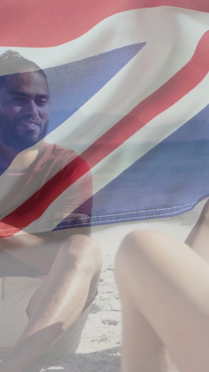 Video verticale: Uomo che sorride a una battuta di un amico in spiaggia, il vento che fa sventolare una bandiera trasparente sull'obiettivo, marketing