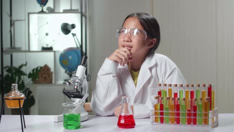 young scientist girl looking at microscope and thinking in laboratory experiment with liquid