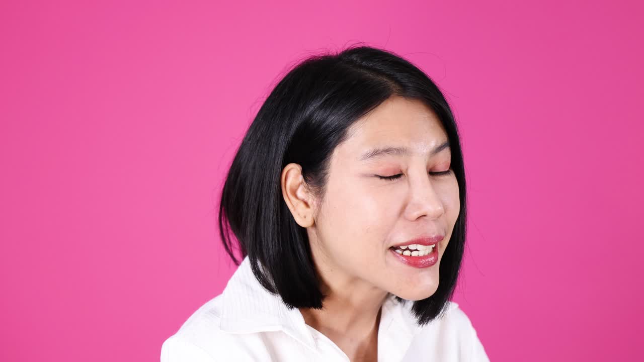 Asian woman in white shirt explains with gestures, expressive face, studio lighting, pink background
