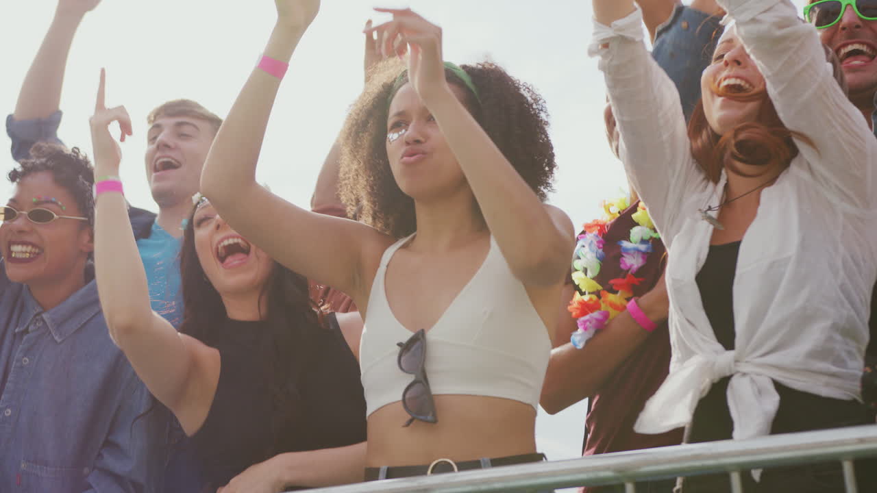 Gruppe unge venner danser bag en barriere ved en udendørs musikfestival